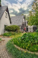 Uma casa tradicional com um caminho de pedra que leva à entrada, cercada por vegetação exuberante e plantas floridas.