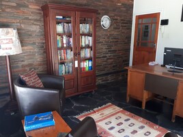 Uma sala de estar acolhedora com poltrona de couro, escrivaninha de madeira, estante de livros e um tapete estampado.