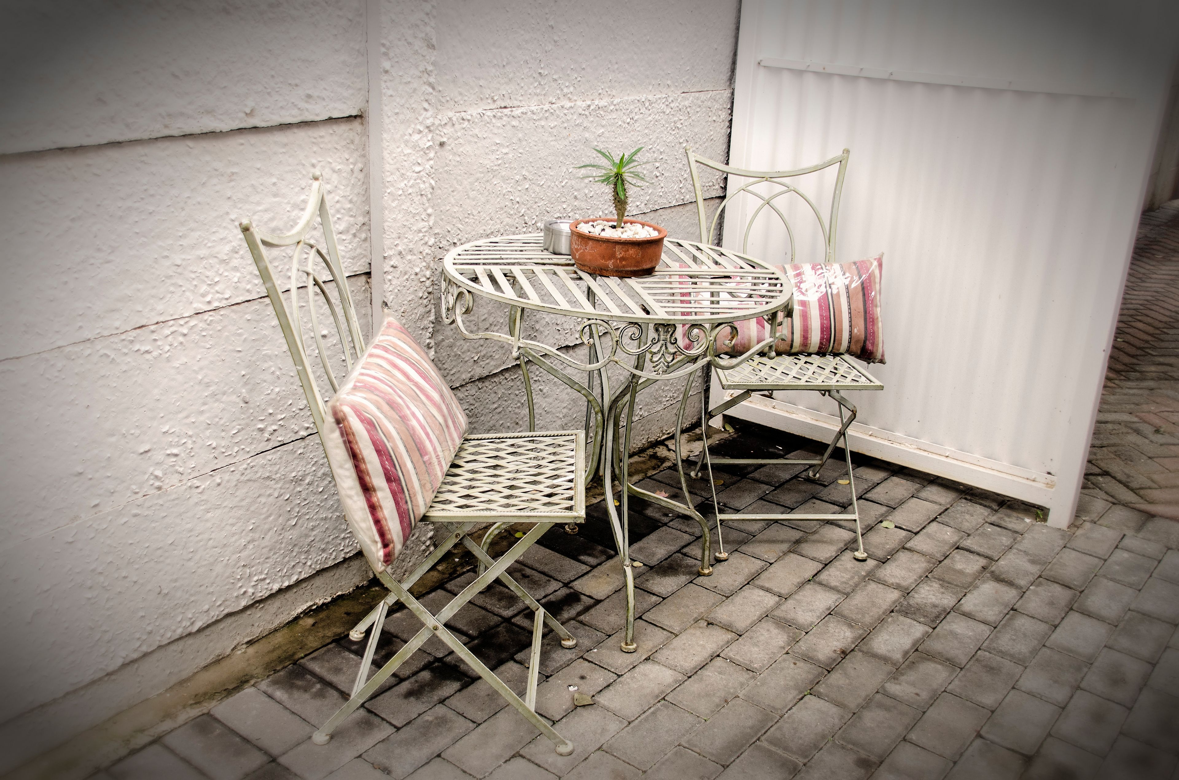 A small outdoor patio with a round metal table and two metal chairs, one with a striped cushion.