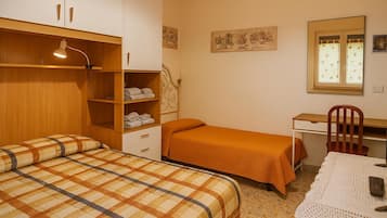 A bedroom with two beds, a desk, a chair, and a table with a remote control.