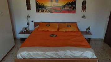 A bedroom with a wooden bed, orange bedding, and a painting of a sunset scene on the wall.