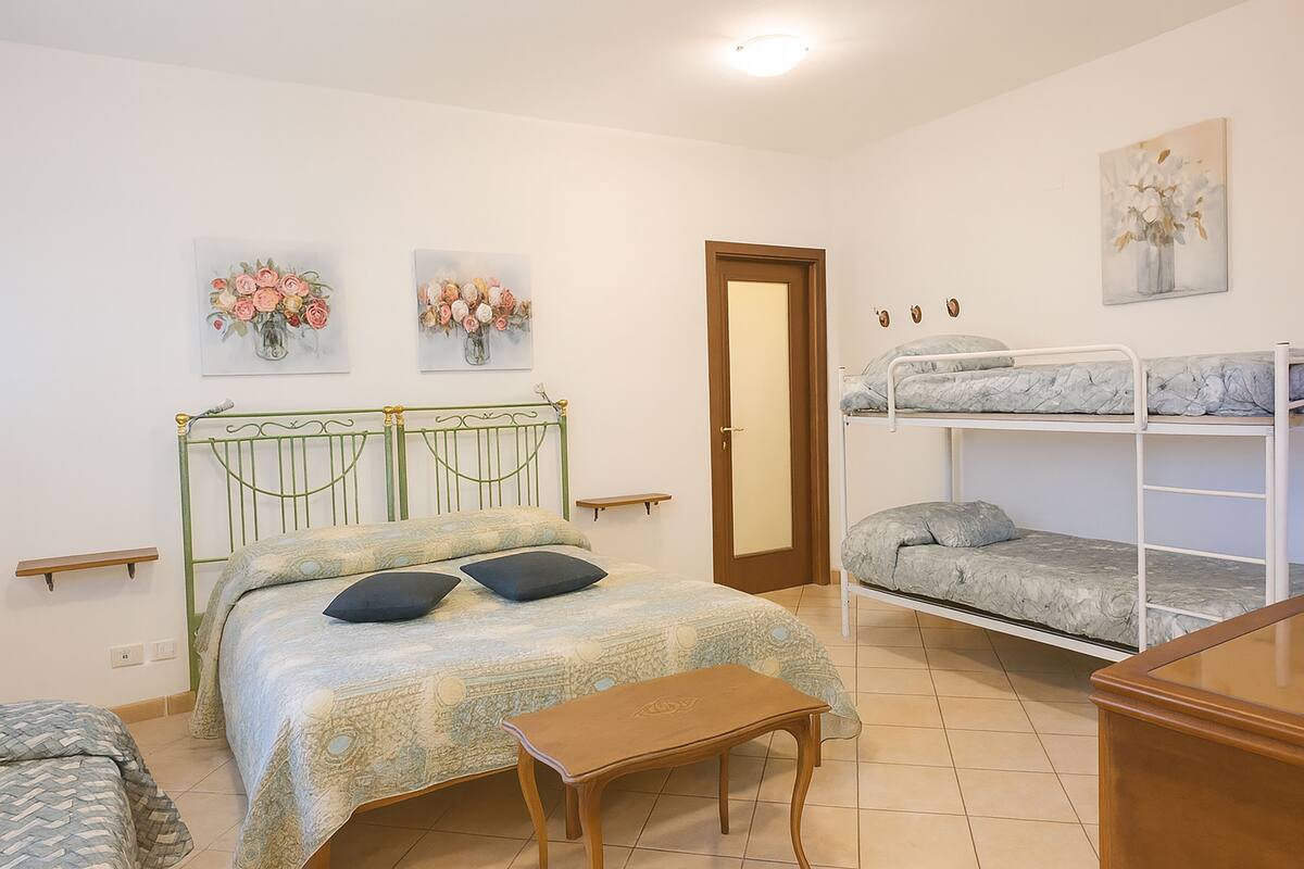 Ein Schlafzimmer mit einem Einzelbett, einem Etagenbett, einem Holztisch und zwei Wandregalen.