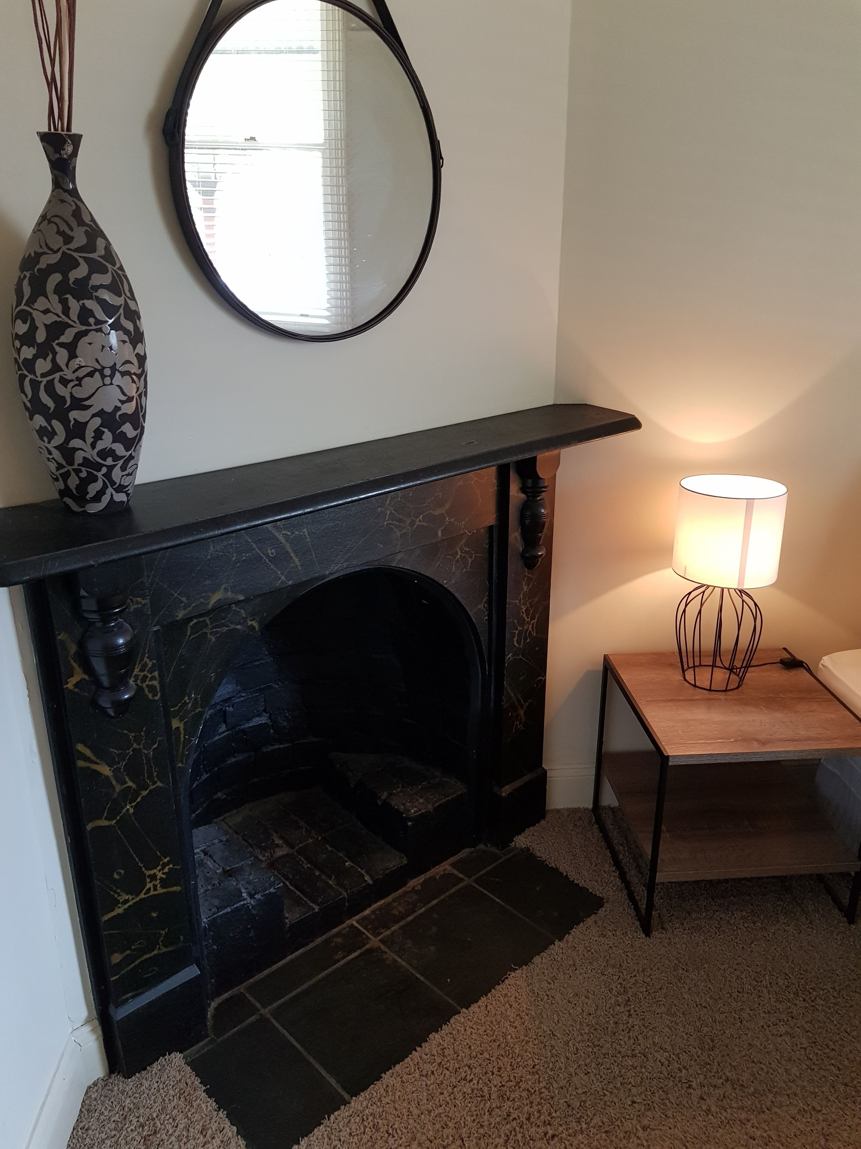 A fireplace with a black mantel, a vase, and a mirror on the wall.