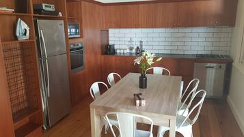 Una cocina compacta con gabinetes de madera, un refrigerador de acero inoxidable, un horno, un microondas, una estufa a gas y un lavavajillas. Hay una mesa de comedor con sillas blancas y un florero con flores.
