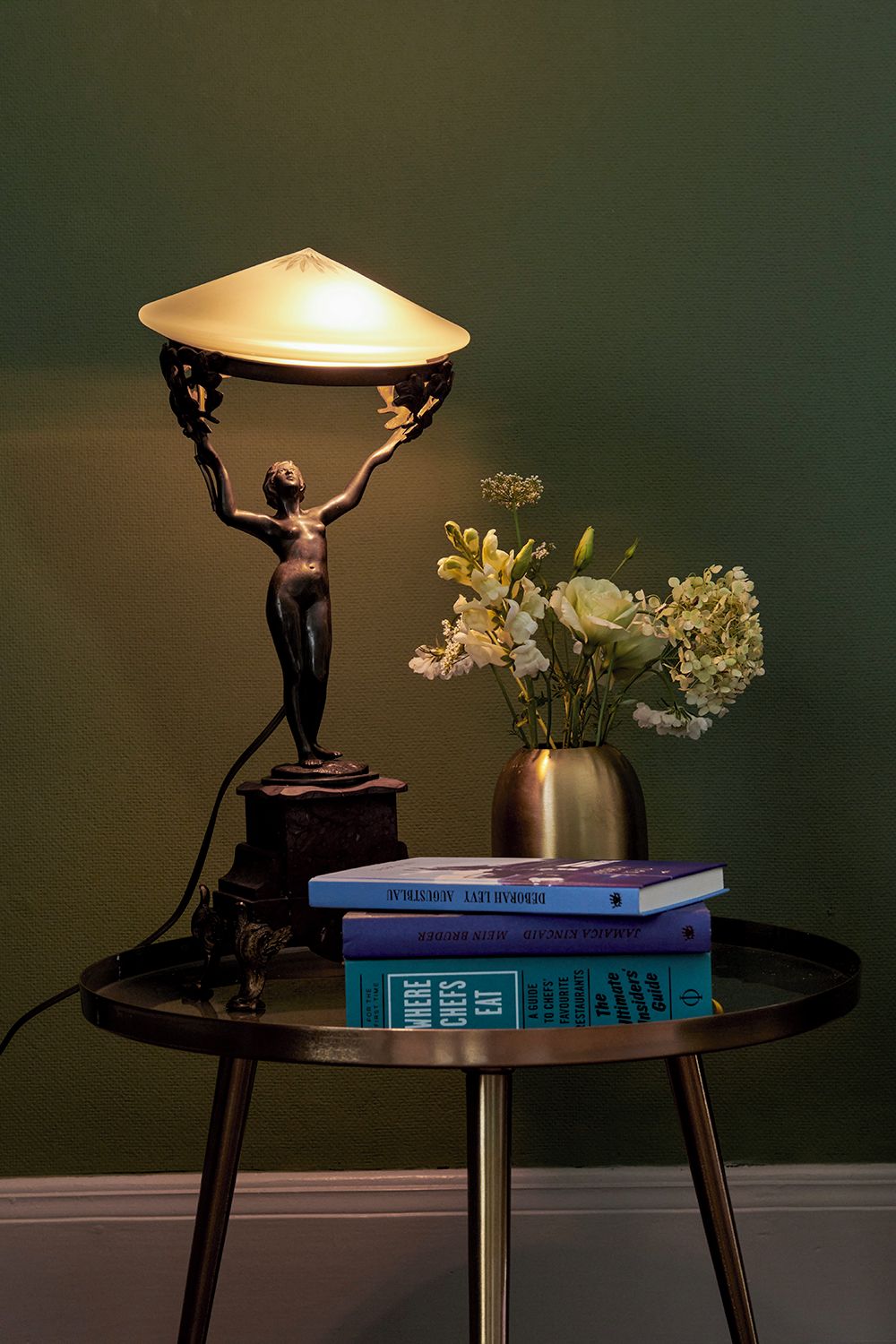 A table with a statue, a vase with flowers, and stacked books.