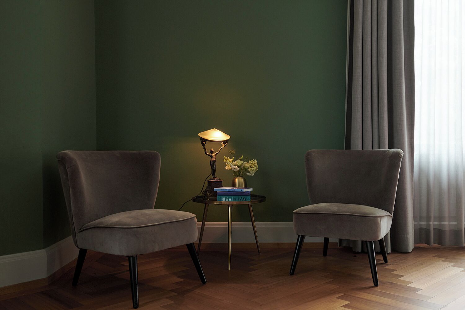 Ein Zimmer mit zwei grauen Sesseln, einem kleinen Beistelltisch mit Lampe und einer Vase mit Blumen.