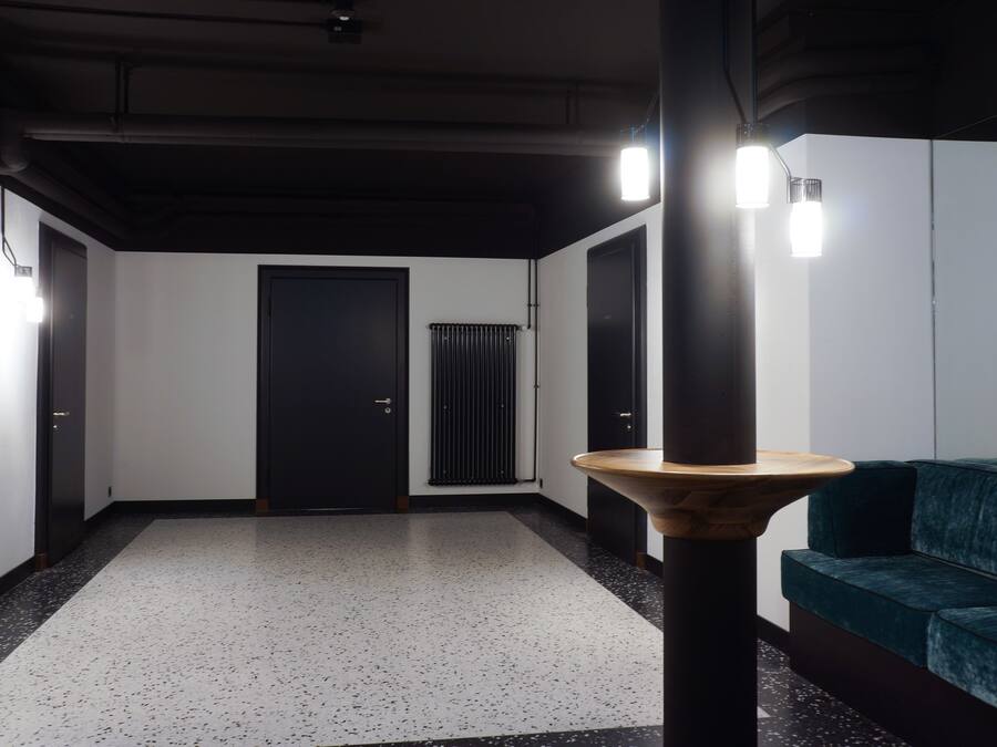 Un pasillo con piso moteado, una mesa de madera, un sofá verde y una puerta.