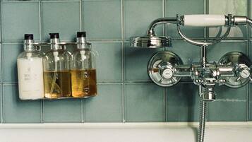 Une salle de bain avec un mur carrelé, une douche et trois bouteilles de liquide sur une étagère.
