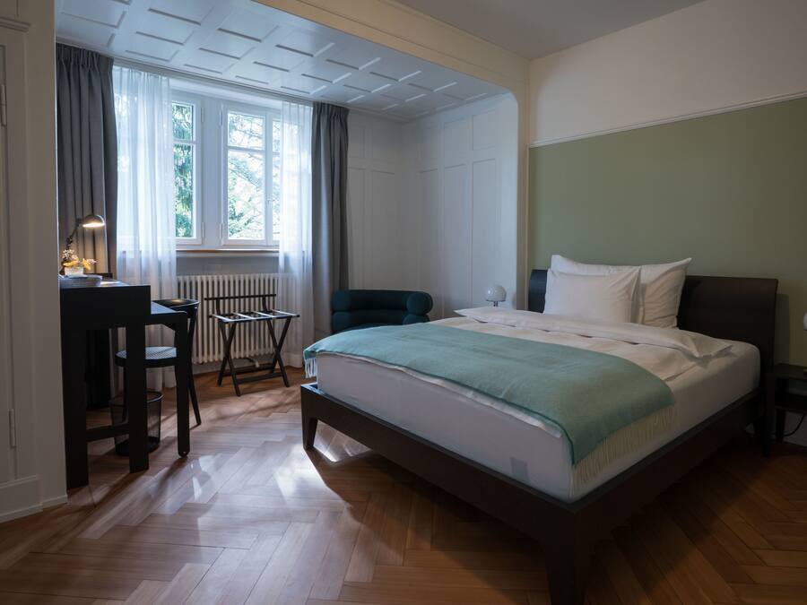 A bedroom with a bed, a desk, a chair, and a radiator.