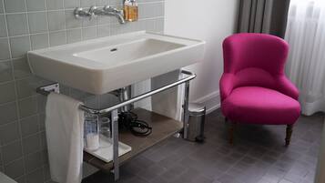 Un baño con un lavamanos blanco, un espejo, un perchero y una silla rosa.