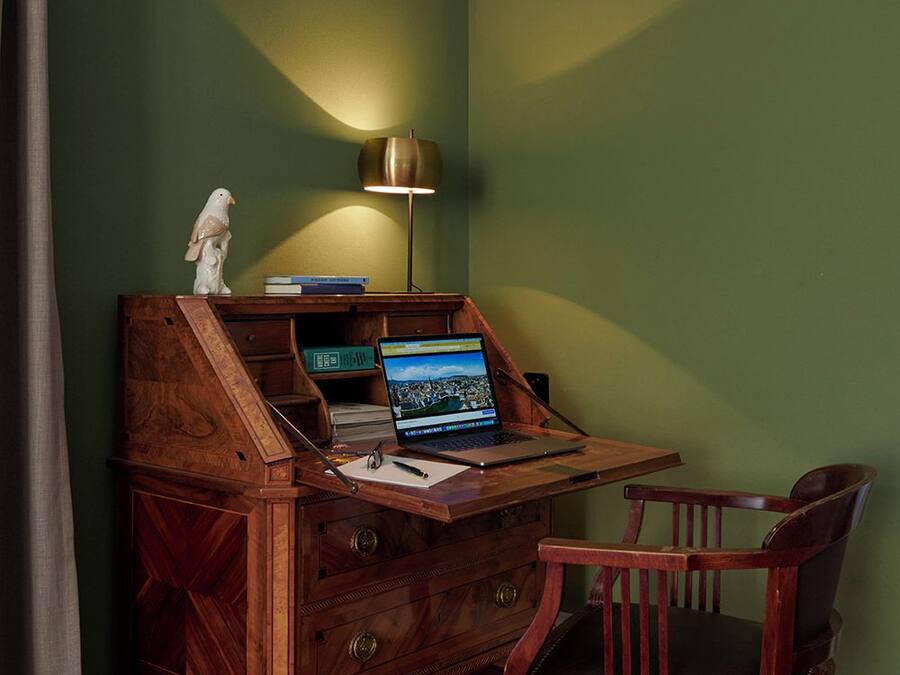 A wooden desk with a laptop, a lamp, and a chair in a room with green walls.