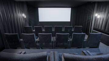 A dark-themed cinema room with rows of black upholstered seats and a large screen at the front.
