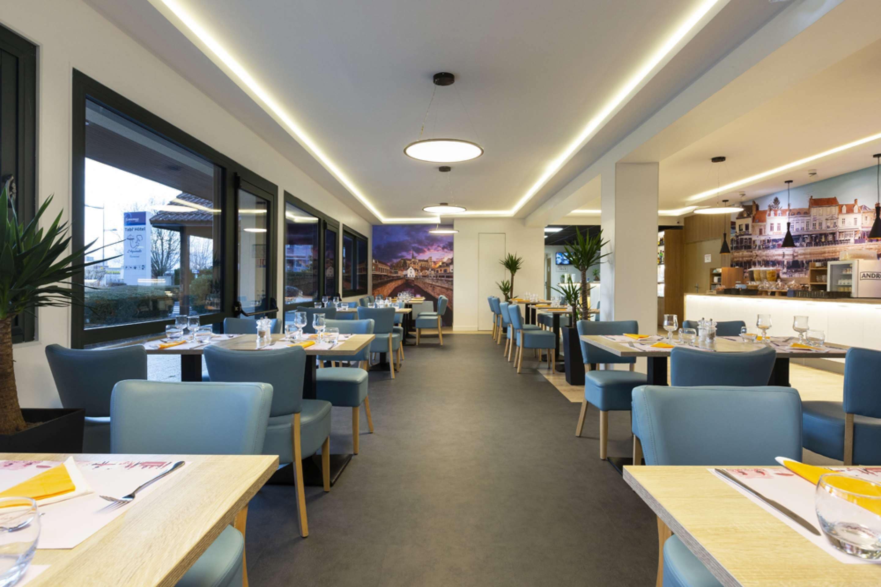 A modern restaurant with a long counter, blue chairs, and a cityscape mural on the wall.