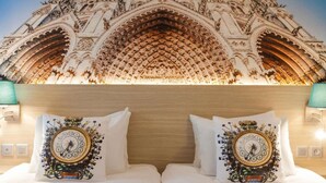 Una habitación de hotel con un techo grande y ornamentado y dos almohadas decorativas con diseños de relojes.