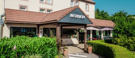 A hotel entrance with a reception area, a covered walkway, and outdoor seating.