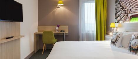 Una habitación de hotel con una cama, un escritorio, una silla, un televisor y una lámpara en la pared.