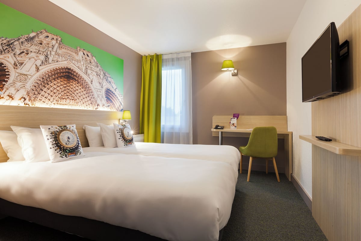 Habitación de hotel con una cama grande, un escritorio, una silla, un televisor y un adorno en la pared.