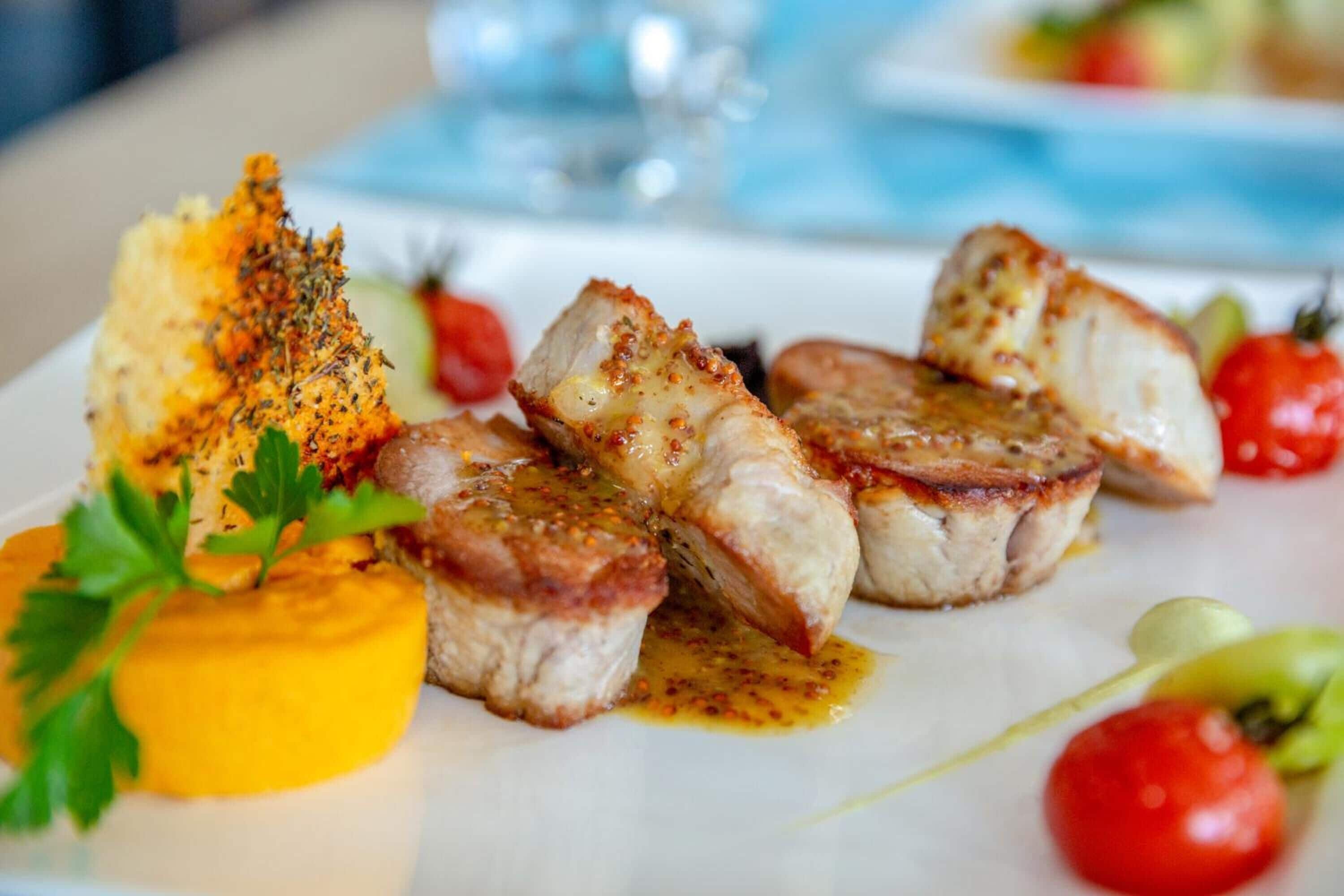 A plate of food with grilled meat, a yellow sauce, and cherry tomatoes.