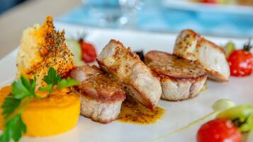 A plate of food with grilled meat, a yellow sauce, and cherry tomatoes.