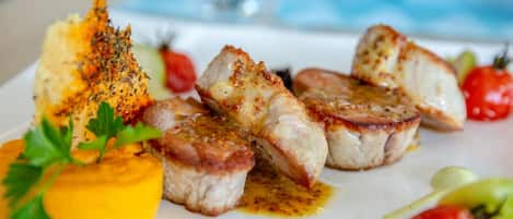 A plate of food with grilled meat, a yellow sauce, and cherry tomatoes.