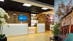 Zona de recepción de un hotel con diseño moderno, un mostrador de recepción, una zona de bar con una variedad de botellas y un mural que representa un edificio tradicional.