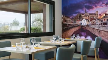 Un restaurant avec des tables dressées pour le service, une grande fenêtre et une fresque représentant un paysage urbain.