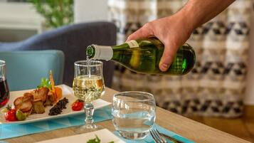 A dining table with a plate of food, a glass of white wine, and a bottle of wine being poured.