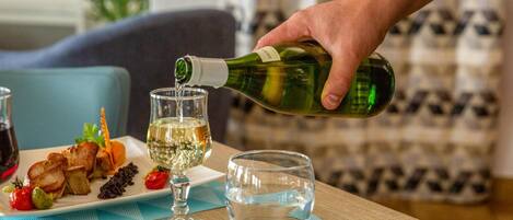 Una mesa de comedor con un plato de comida, una copa de vino blanco y una botella de vino siendo servido.