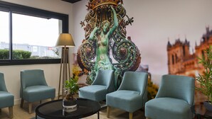 Una habitación con cuatro sillones turquesa, una mesa redonda negra con una planta en maceta y un mural decorativo grande.