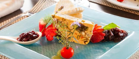 Un plato de comida con una variedad de elementos, incluyendo una porción de quiche, tomates cherry, uvas y hierbas aromáticas.