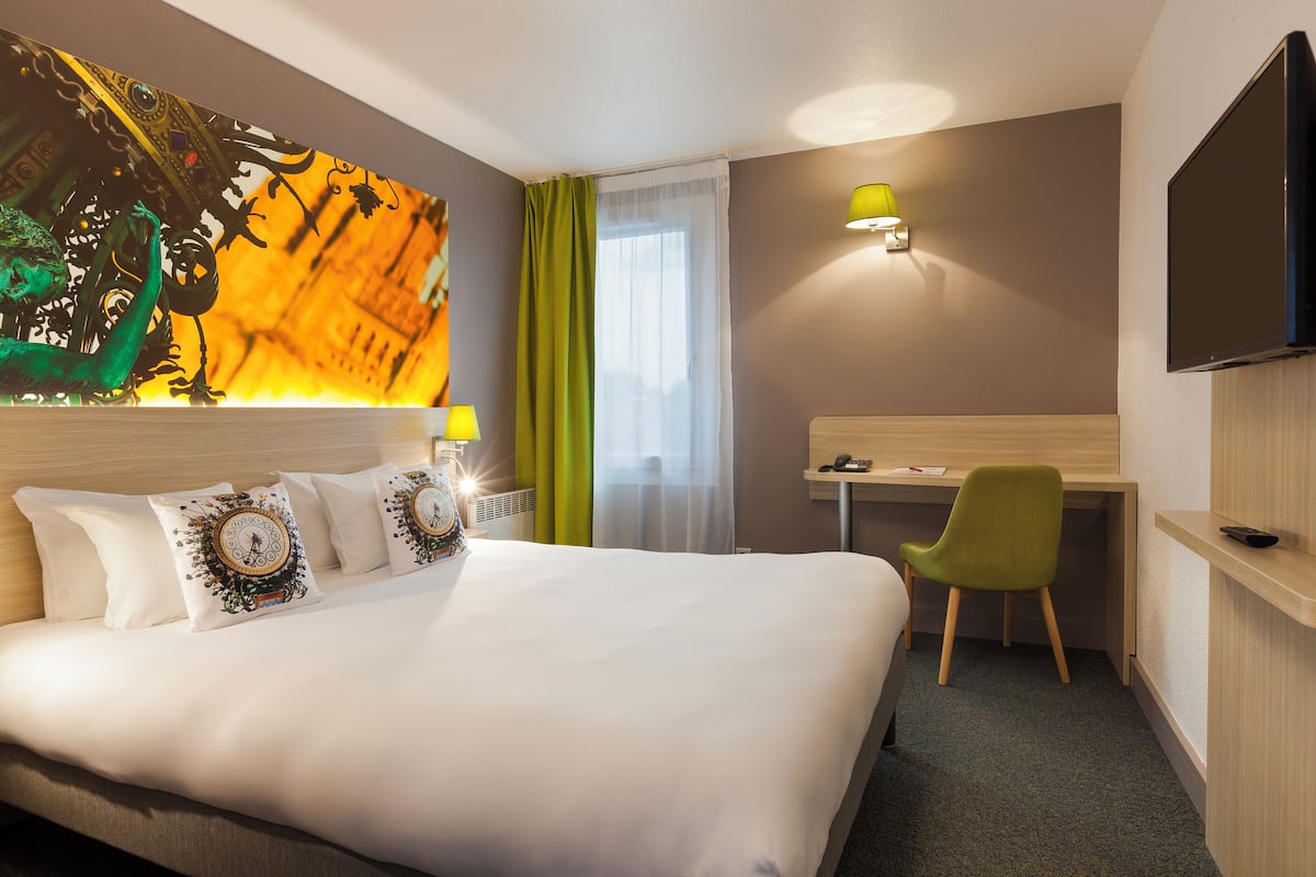 Habitación de hotel con una cama grande, un escritorio, una silla, un televisor y un cuadro en la pared.