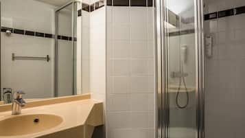 Un baño con lavamanos color crema, cabina de ducha de vidrio y paredes con azulejos blancos.
