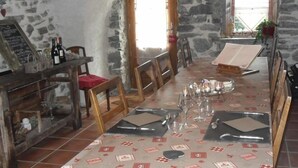Un coin repas rustique avec des murs en pierre, une table en bois dressée pour deux personnes et un meuble à vin rempli de bouteilles.