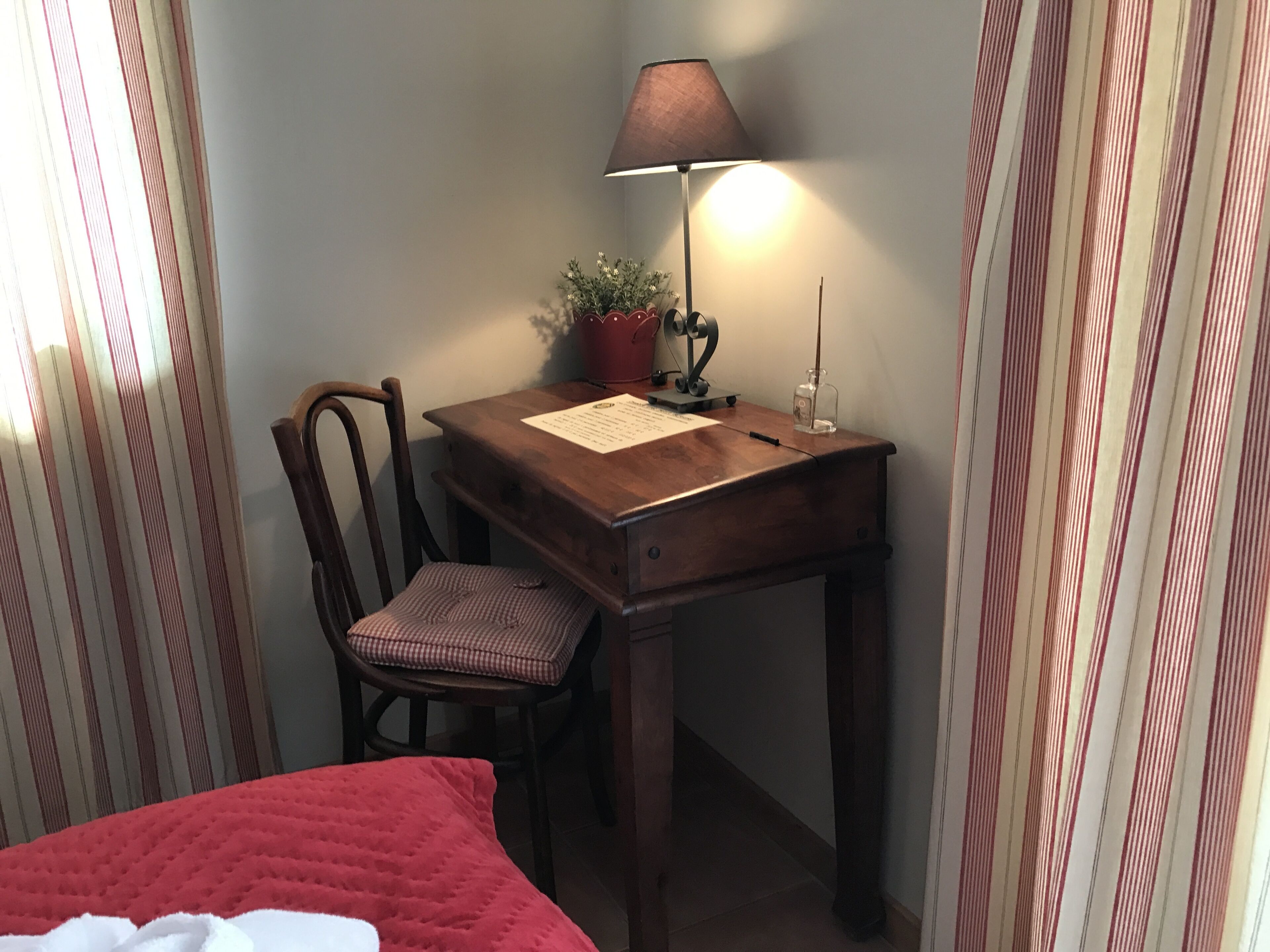 Un bureau en bois avec une lampe, une chaise, une petite plante en pot et un document posé sur le bureau.