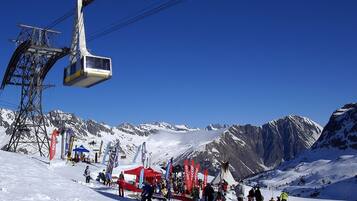 A ski lift with a gondola carrying passengers, a ski slope with people, and a mountainous backdrop.