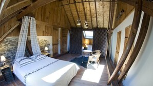 Une chambre confortable avec un grand lit, un bureau et une chaise, agrémentée de poutres en bois et de murs en pierre.