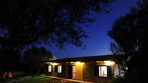 Una casa in pietra con un ingresso ben illuminato e finestre, circondata da alberi e un prato.