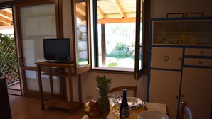 Un'area pranzo con un tavolo apparecchiato per due, una televisione su un mobile e vista sul giardino attraverso una finestra.