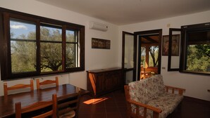 Un'area pranzo con un tavolo e sedie in legno, un divano floreale e ampie finestre vista alberi.