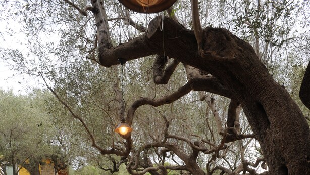 Patio esterno con pareti in pietra, sedie bianche e lampadario.
