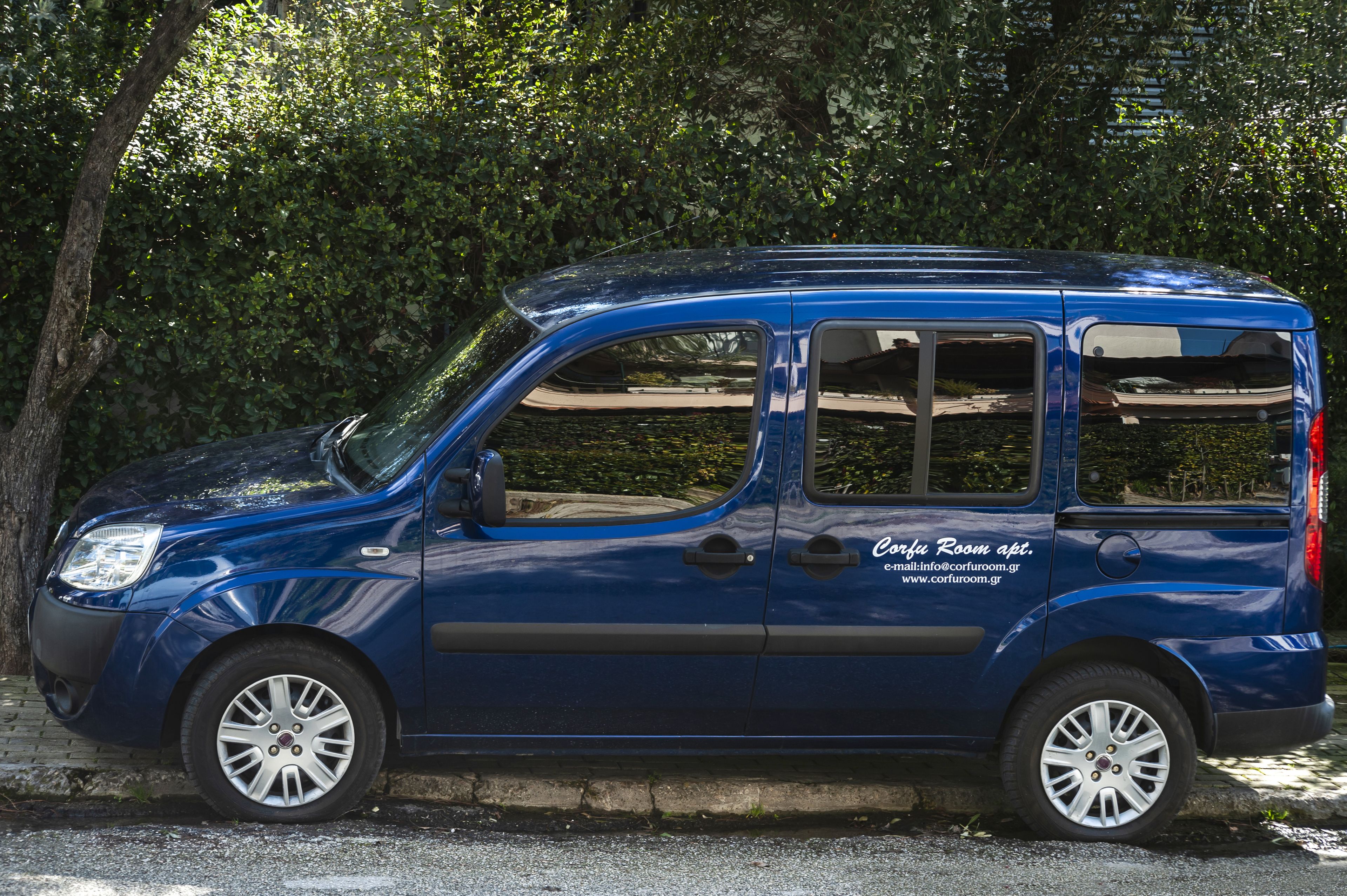 A blue compact car parked on a street with trees in the background.