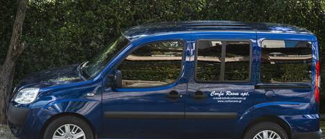A blue compact car parked on a street with trees in the background.
