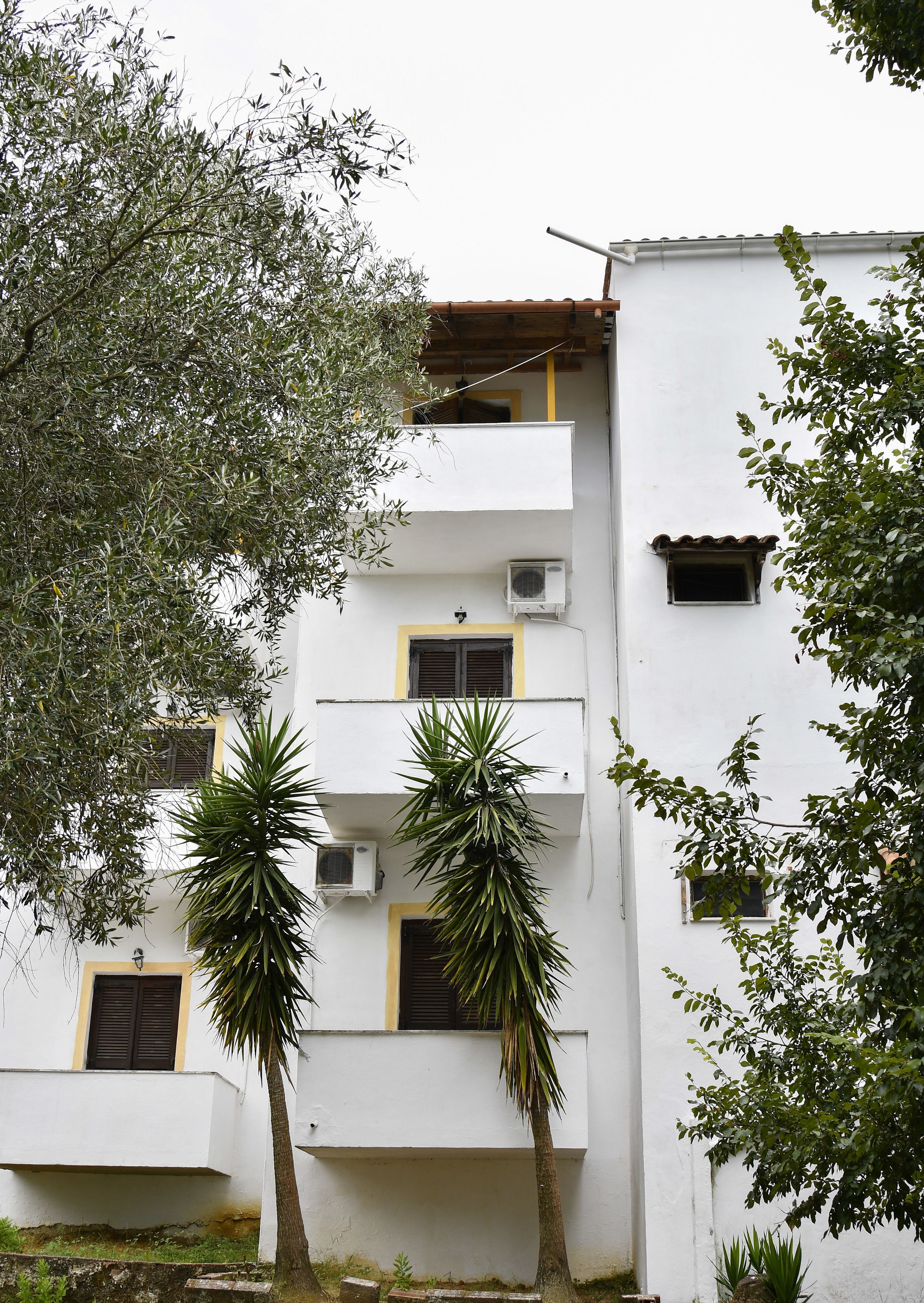 Un edificio blanco con varios balcones, unidades de aire acondicionado y techo de tejas.