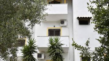 Un edificio blanco con varios balcones, unidades de aire acondicionado y techo de tejas.
