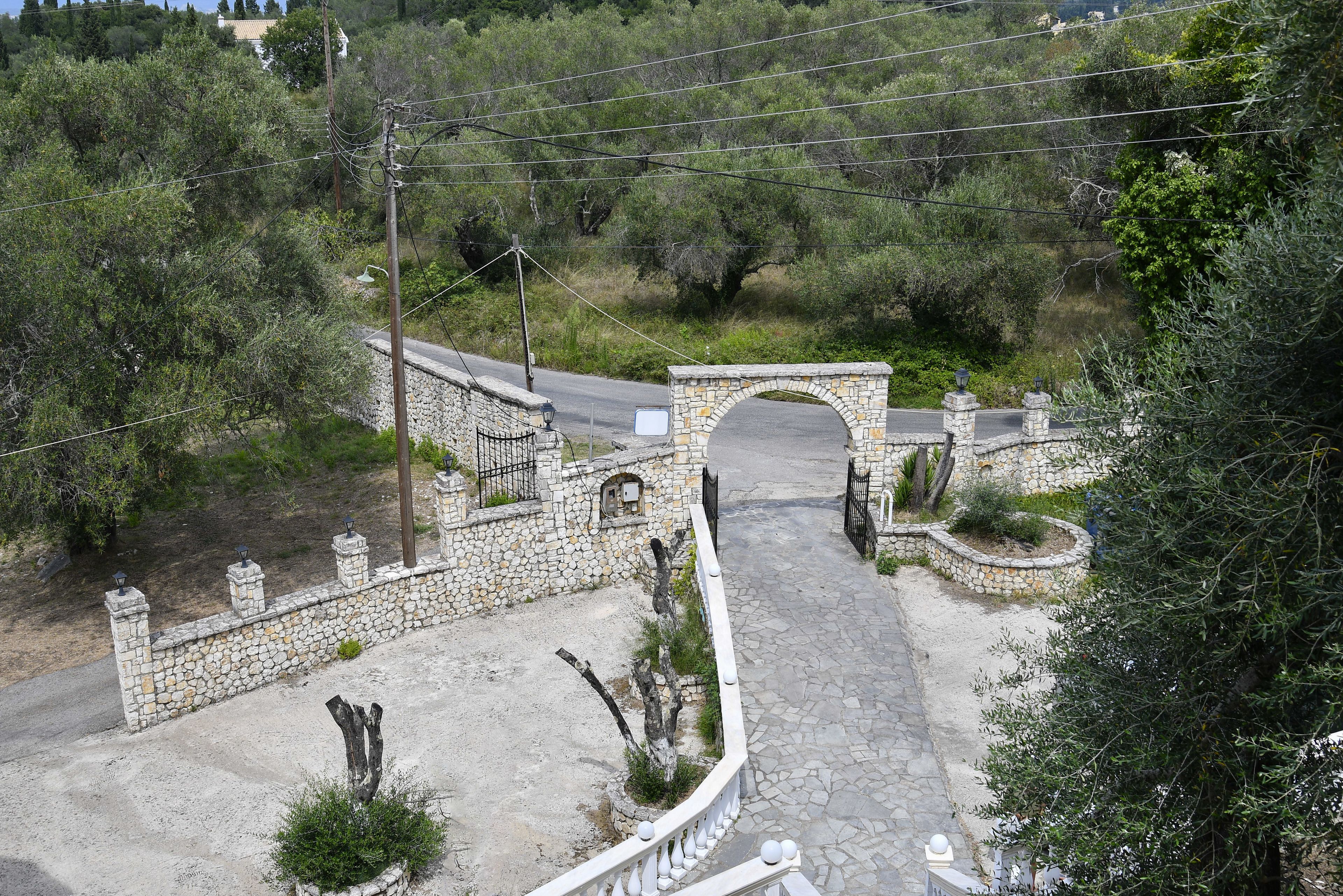 A stone bridge over a paved path, surrounded by greenery and a stone wall with a metal railing.