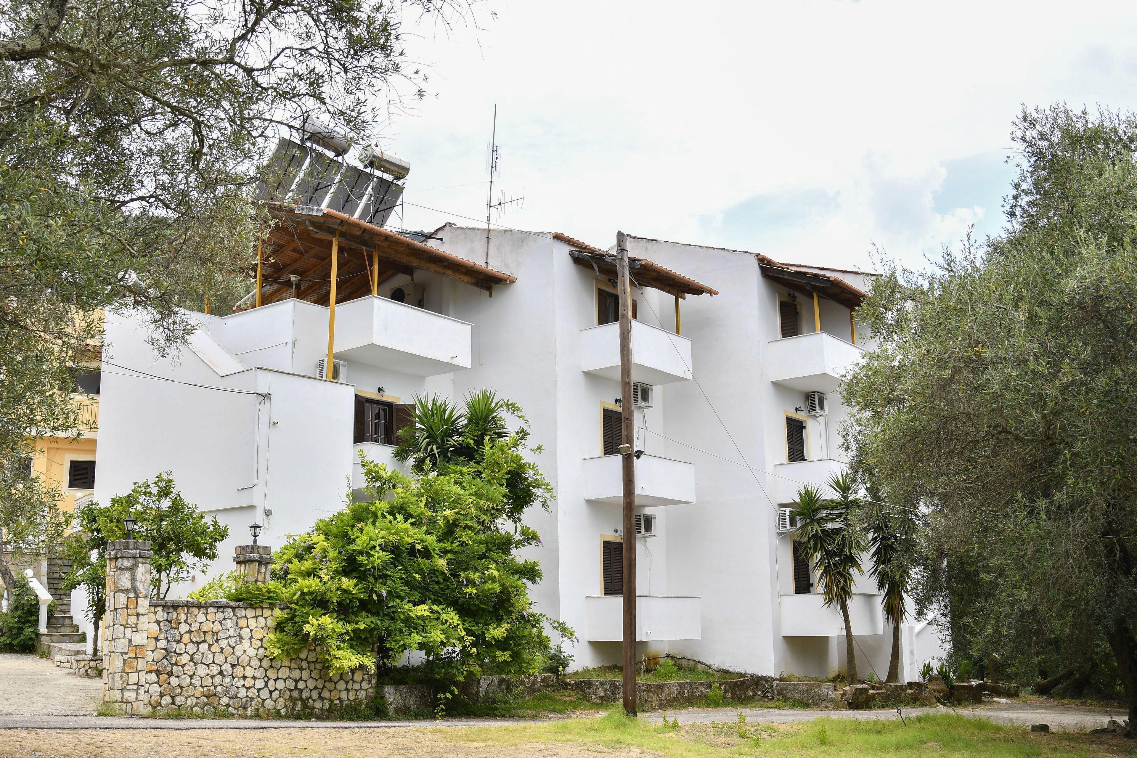 Un edificio bianco a più piani con balconi, un muro in pietra e un pannello solare sul tetto.