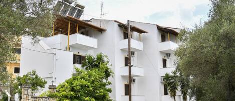 Un edificio bianco a più piani con balconi, un muro in pietra e un pannello solare sul tetto.