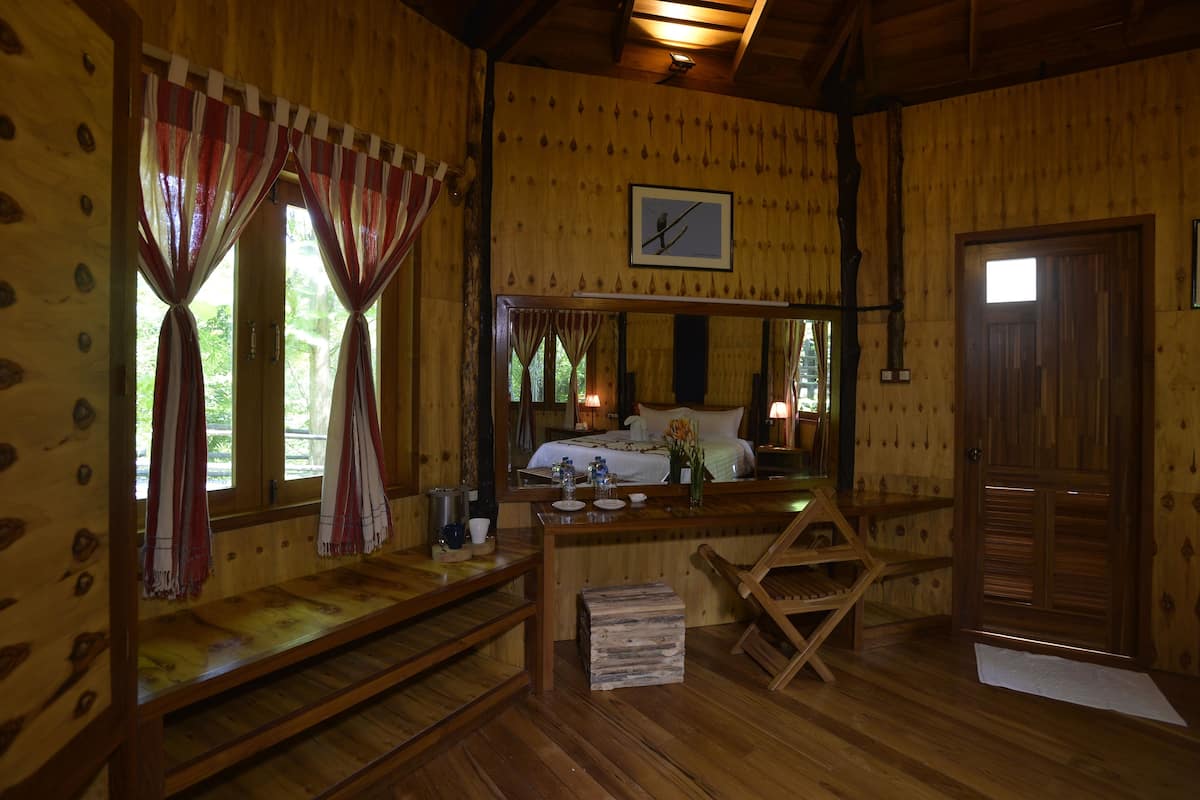 A wooden cabin room with a bed, a wooden bench, a small table with a pitcher, and a mirror on the wall.