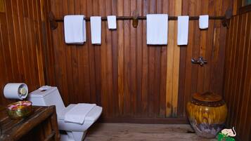 A bathroom with a toilet, towels, and a shelf with a bowl of fruit.