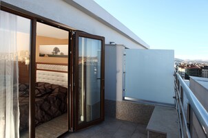 Un balcón con cama, puerta de cristal y vista a la ciudad.